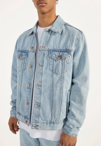 Ljusblå denimjacka med knäppning, två bröstfickor och krage av standardmodell. Har stickningsdetaljer och en avslappnad passform.