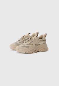 Beige sportovní boty s síťovinou a silnou podrážkou, nakloněné pro viditelnost. Na boku je vystaveno logo značky "Steve Madden".