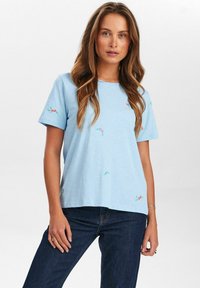 Camiseta de manga corta en azul claro con bordados florales dispersos en rosa y verde, cuello redondo, ajuste relajado y tejido de algodón suave.