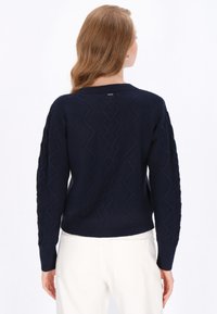 Granatowy sweter dzianinowy z teksturowanym wzorem fal, okrągłym dekoltem i ściągaczami. Posiada subtelną metkę na górze pleców.