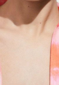 Nahaufnahme einer glatten, hellen Hautoberfläche mit leichtem Glanz, neben weichem Stoff in einem lebhaften pinken und orangefarbenen Batikmuster.