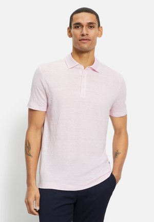 Light pink short-sleeve polo shirt with a soft texture, featuring a classic collar and three-button placket. Model wears navy pants.