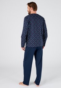 Pigiami blu navy con una parte superiore a maniche lunghe decorata con piccoli ancore bianche e rosse. I pantaloni sono blu navy solidi con una vestibilità comoda.