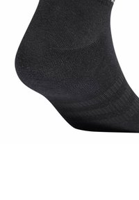 Zbliżenie na piętę czarnej skarpetki, ukazujące szydełkowaną teksturę i wzmocnione szwy na białym tle.