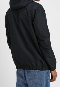Black windbreaker jacket with a hood. Features elastic cuffs and waistband, made of smooth, water-resistant material. Back view shown.