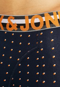 Boxer da uomo blu navy con vita elastica recante la scritta 'JONAK' in arancione. Il tessuto presenta un motivo a pois arancioni e bianchi, con una texture liscia.