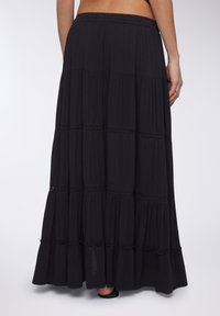 Gonna maxi nera con un design a strati, texture morbida e dettagli ricamati lungo le cuciture. Vita elastica per una vestibilità comoda.