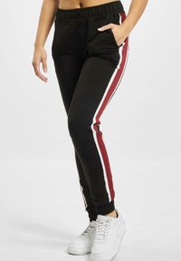 Sorte joggebukser har en innsnævret design med elastisk liv. De har hvite og burgunder sidestriper og sidelommer.