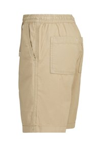 Beige-shortsit, joissa on elastinen vyötärö, sivutaskut ja takatasku. Valmistettu pehmeästä ja kestävästä kankaasta, joka tuntuu sileältä.