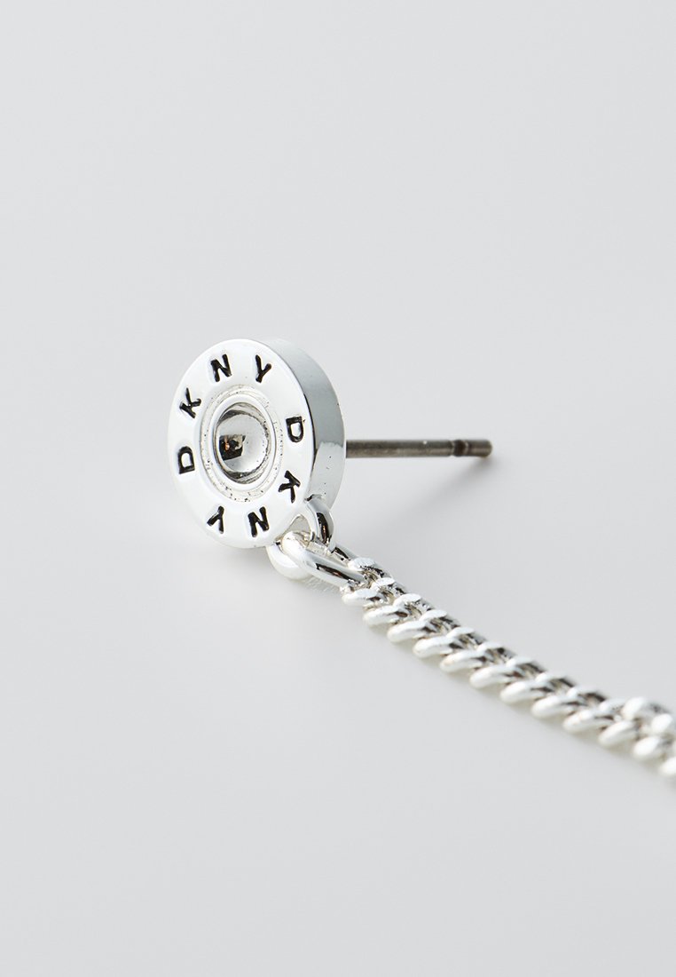 Srebrna kolczyk z okrągłym wkrętem z napisem "DKNY" i elementem łańcuszka, zaprezentowany z wypolerowaną powierzchnią i eleganckim designem.