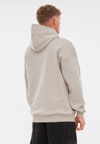 Jasnoszara bluza z kapturem, z kieszenią kangurzą, w oversize'owym kroju i prążkowanymi mankietami. Wykonana z miękkiej bawełny, z regulowanym kapturem i minimalną liczbą szwów.