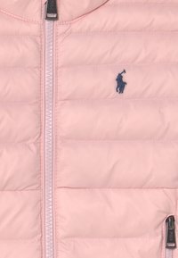 Vadderad rosa jacka med dragkedja framtill, med marinblå logotyp, horisontell sömnad och en slät, matt yta.