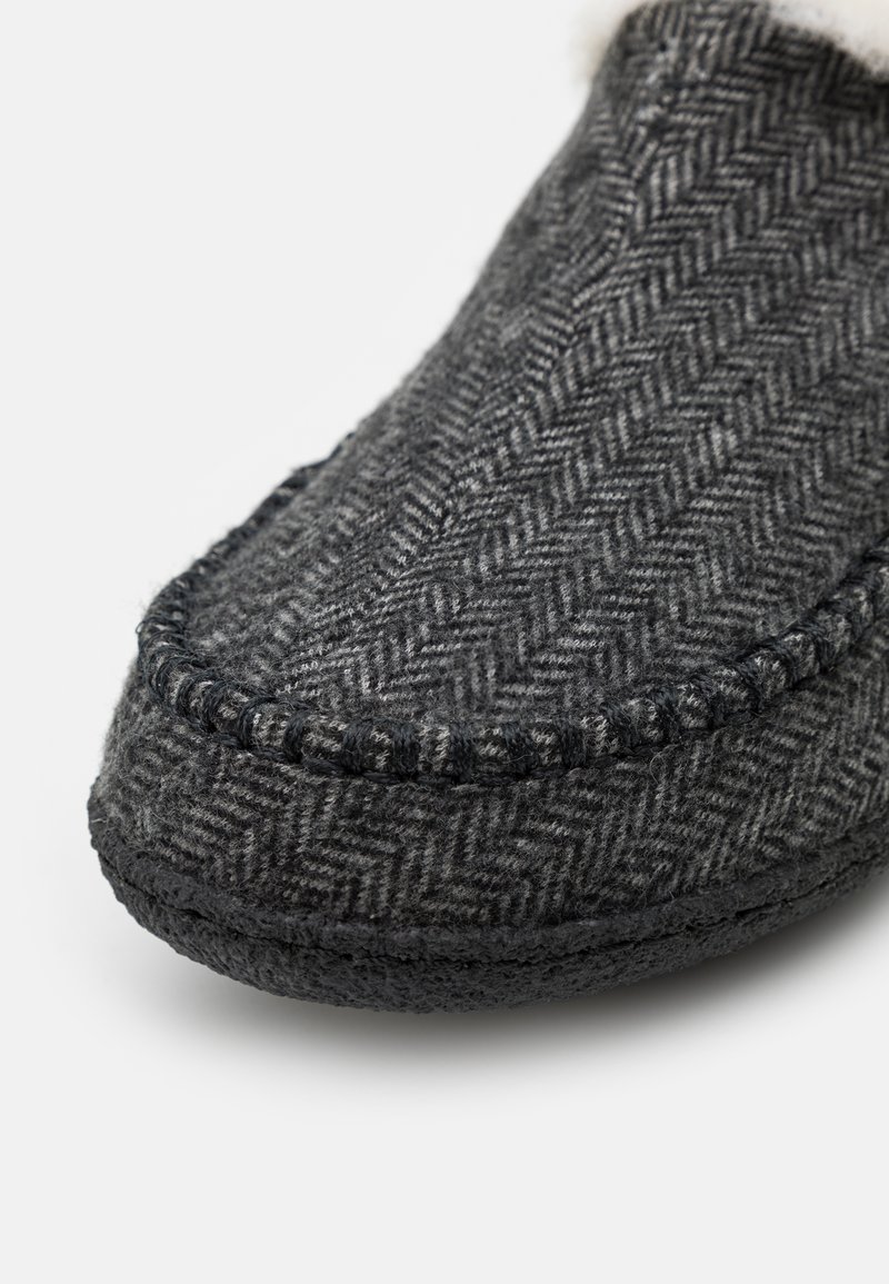 Zapatilla de lana gris con un patrón de espiga, puntera redondeada, suela de goma negra y costuras en contraste a lo largo del borde.