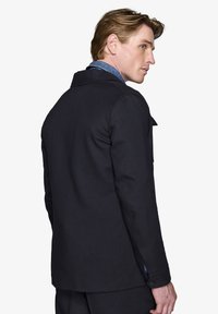 Sort frakke med en skræddersyet pasform, tekstureret stof, skåret krave og knapmanchetter. Har en denimdetalje, der er synlig ved kraven.