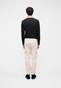 Μαύρο πουκάμισο με μακριά μανίκια, μπεζ παντελόνι cargo με ελαστικά μανσέτες, τσέπες με πατς και μαύρα παπούτσια, από πίσω.