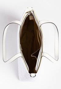 Valkoinen tilkkupussukka, jossa on kaksinkertaiset olkahihnat, avoin vetoketju, joka paljastaa ruskean sisävuoren ja sisätaskut, valkoista taustaa vasten.