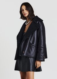 Giacca di pelle nera con collo in shearling, dotata di un design doppiopetto, due tasche frontali e una vestibilità leggermente cropped.