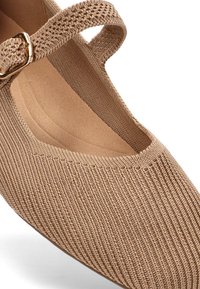 Zapato Mary Jane de tela color beige con textura ribeteada, puntera redonda y una correa tono a tono con un acento de hebilla dorada.