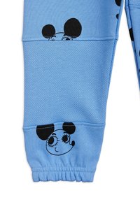 Blå träningsbyxor i texturerad tyg med svarta cartoon-musans ansikten vid knäna och elastiska muddar.