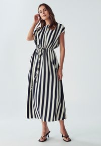 Tummansininen ja kerma-valkoinen raidallinen maksimekko, joka on rento istuvuudeltaan, kerätty vyötärö sidottavalla vyöllä ja lyhyillä hihansuihin. Suora kangas.