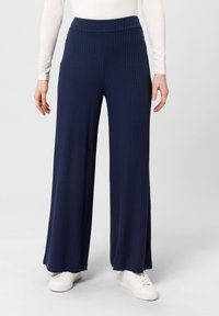 Pantalones de pierna ancha, de color azul marino y con canalé, con una cintura alta, fabricados en una tela suave, combinados con zapatillas blancas para un look casual.