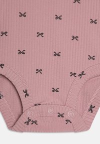 Rózsaszín bordázott body, szétszórt fekete masni mintával, vékony mandzsettákkal és kényelmes patentokkal az alján a könnyű öltözködés érdekében.