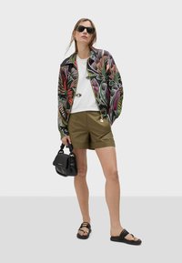 Šarena bomber jakna s cvjetnim uzorkom, bijela majica, maslinaste kratke hlače, crna torba i crne sandale s zlatnim detaljima.