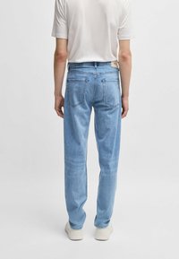 Jeans in denim azzurro chiaro con taglio dritto, cinque tasche e dettagli di cucitura sul retro, abbinati a una maglietta bianca semplice e scarpe chiare.