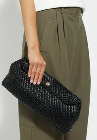 Black woven leather clutch bag with a curved shape, featuring a gold button closure and textured surface, held in a hand.
