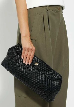 Zwarte geweven leren clutch met een gebogen vorm, voorzien van een gouden knoopsluiting en een gestructureerd oppervlak, vastgehouden in een hand.