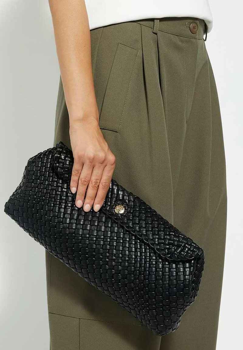 Black woven leather clutch bag with a curved shape, featuring a gold button closure and textured surface, held in a hand.