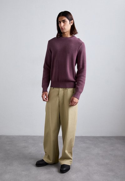 Burgundi kötött pulóver ribbelt nyakkal és mandzsettákkal, laza bézs nadrággal és fekete slip-on cipőkkel párosítva. Minimális design, sima textúra.