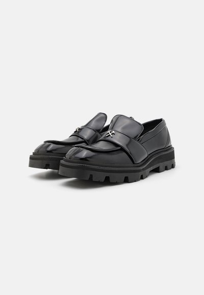 Black patent leather shoes with a chunky rubber sole, featuring a wide strap across the top and a small metallic accent detail.