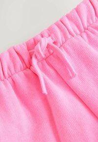 Des sweatpants en coton rose dotés d'une taille élastique avec un cordon de serrage. Le tissu est doux avec une texture lisse.