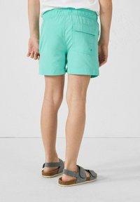 Turquoise shorts met een comfortabele elastische tailleband en grote achterzak, gecombineerd met grijze sandalen met een kurken zool en bandontwerp.