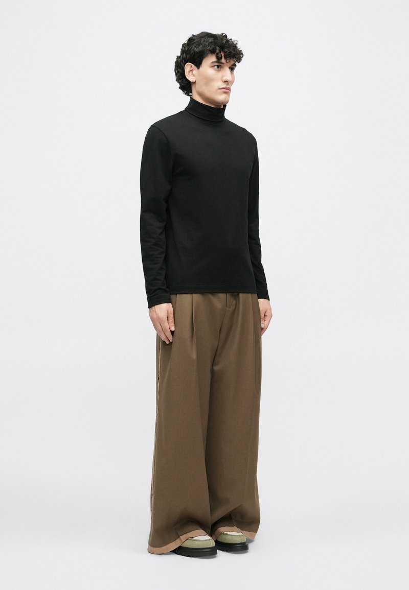 Sort langærmet turtleneck i kombination med løse brune bukser. Bemærkelsesværdige træk inkluderer en glat tekstur og vidde ben-design.