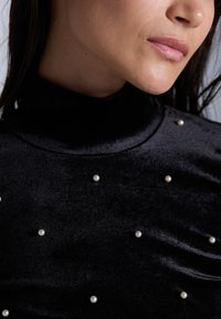 Svart fløyels turtleneck topp pyntet med jevnt fordelte små perler, som viser en glatt tekstur og en tettsittende design.