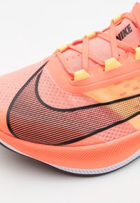 Chaussure de running Nike en rose vif et orange, avec un swoosh noir, une tige en mesh, un motif texturé et des accents jaunes au niveau des lacets.