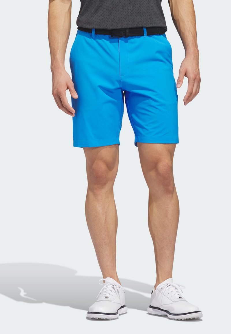Herren-Shorts in Blau aus leichtem Material mit elastischem Bund und Seitentaschen, kombiniert mit weißen Golfschuhen mit schwarzen Akzenten.