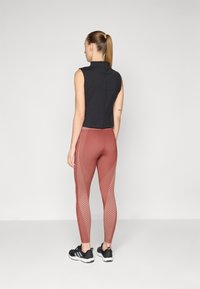 Un haut sans manches noir associé à des leggings brun rougeâtre illustrant des motifs géométriques. Porté avec des chaussures de sport noires, vu de dos.
