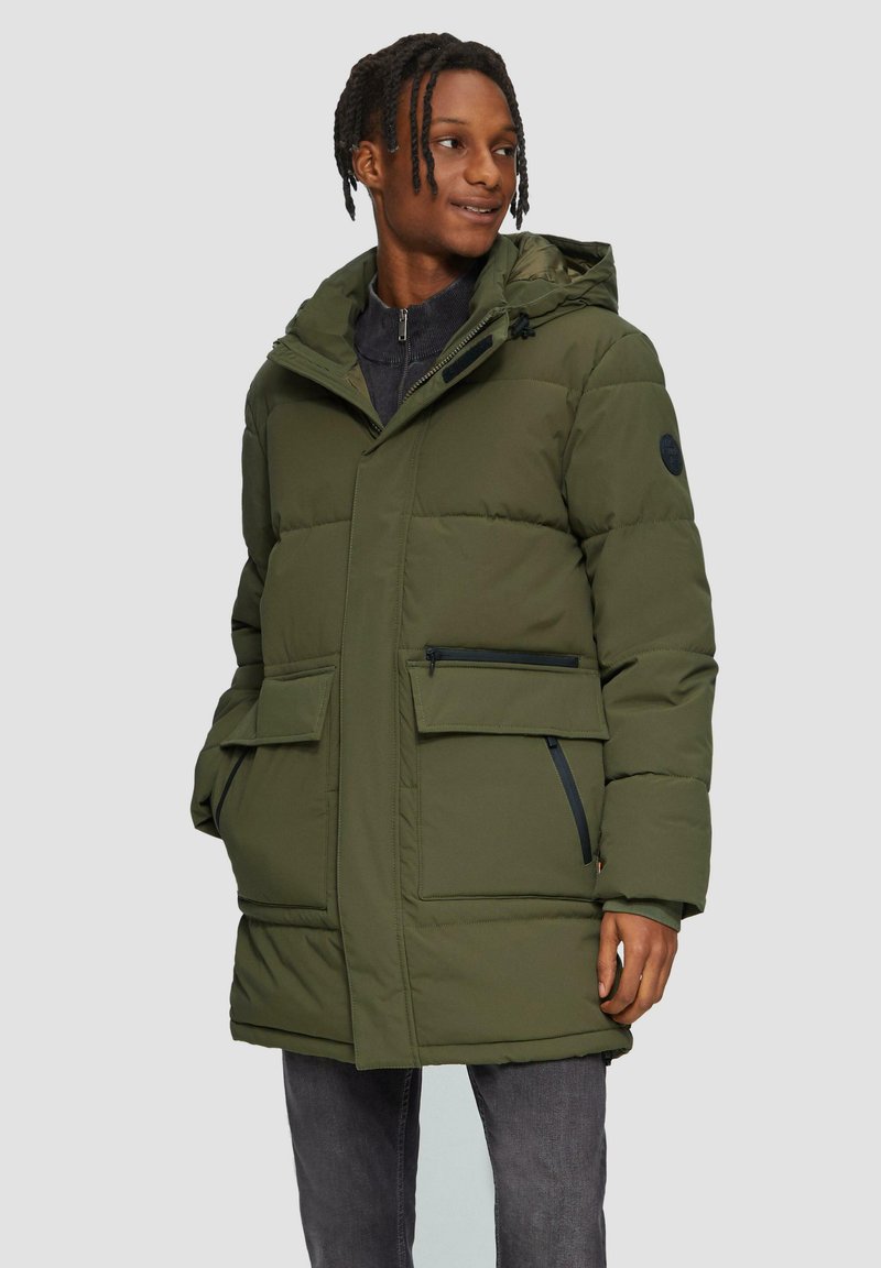Veste matelassée en vert olive avec capuche, dotée d'une fermeture éclair, de deux poches avant et d'un design angulaire. Tissu texturé avec rembourrage.