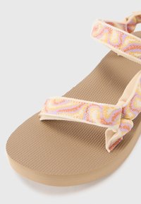 Flat sandal featuring a textured brown sole, with multicolored floral-patterned straps and a smooth, light-colored toe post.