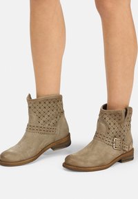 Botas de tobillo de ante color tan con detalles perforados, superficies texturizadas, una correa decorativa y un tacón bajo apilado.