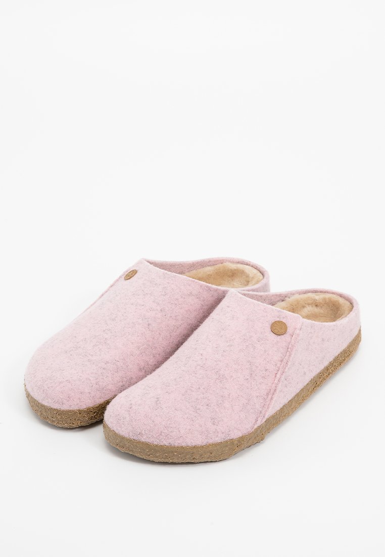 Chaussons en feutre rose clair avec une surface texturée, bout rond et doublure douce. Semelle en liège avec un petit bouton décoratif sur le côté.