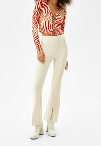 Maglia a maniche lunghe a righe rosse e crema con scollatura lacciata; abbinata a pantaloni a vita alta color crema a campana e tacchi bianchi chunky.