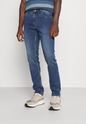 Tynne blå jeans laget av denim, med fem lommer og kontrastsøm, parret med beige joggesko.