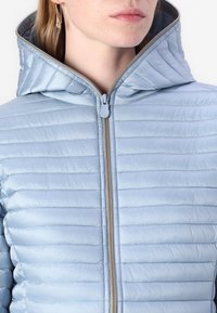 Lyseblå pufferjakke med horisontale syninger, høj krave og en frontlynlås med gyldent hardware. Glat tekstur, ingen mønstre.