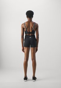 Reggiseno sportivo nero con spalline decorate con logo, abbinato a pantaloni sportivi neri a vita alta. Tessuto liscio con una vestibilità attillata.