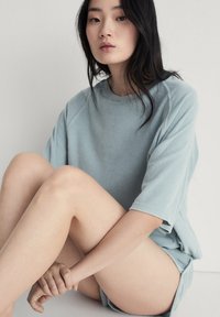 Lichtblauwe oversized sweatshirt met een zachte textuur, voorzien van korte mouwen en een ronde halslijn, gecombineerd met eenvoudige lichte shorts.