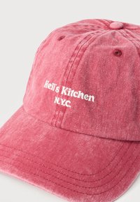 Κατεστραμμένο κόκκινο καπέλο του μπέιζμπολ με λευκή κεντητή επιγραφή "Hell's Kitchen N.Y.C." στο μπροστινό πάνελ.